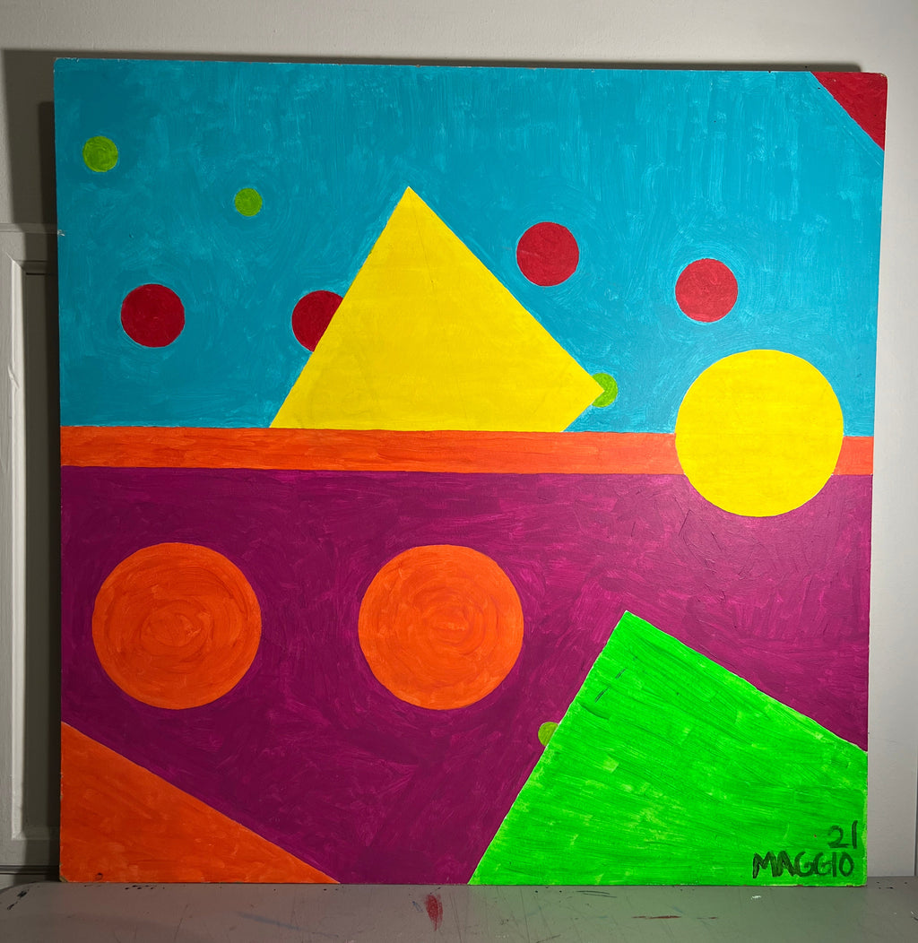 A colorful abstract geometric painting on canvas, featuring bright shapes in blue, purple, green, orange, yellow, and red, photographed leaning against a wall in an indoor space.